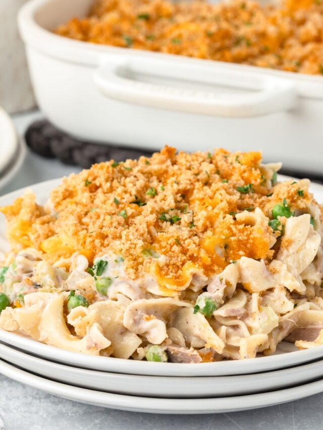 Tuna noodle casserole with cheese and breadcrumbs served on a white plate.