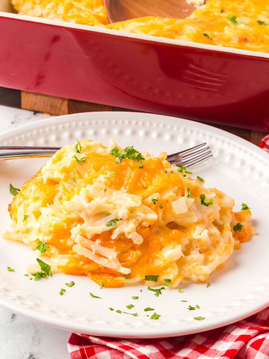 Cracker barrel hashbrown casserole served on a white plate with a fork. A cheap potluck dish to bring to a church gathering.