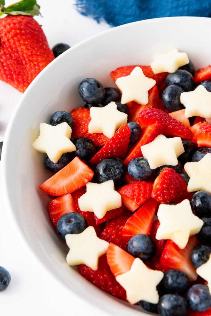 Rd white and blue fruit salad in a white bowl.