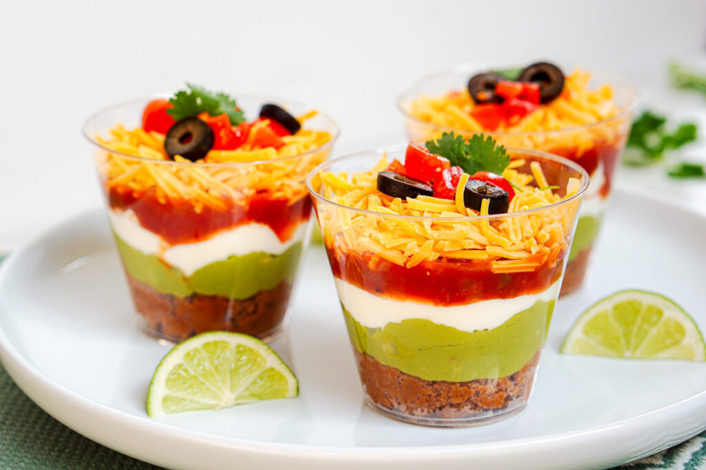 7 Layer taco dip in cups sitting on a plate.
