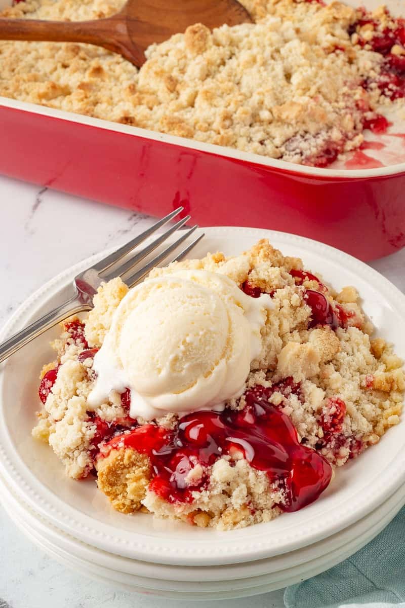 Cherry dump cake with vanilla ice cream on white plate with fork.