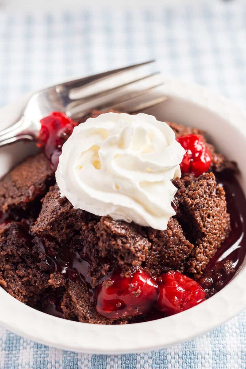 Chocolate cherry dump cake with a dollop of whipped cream in white bowl with fork.