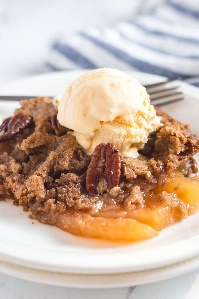 Apple dump cake on white plate with a scoop of vanilla ice cream.