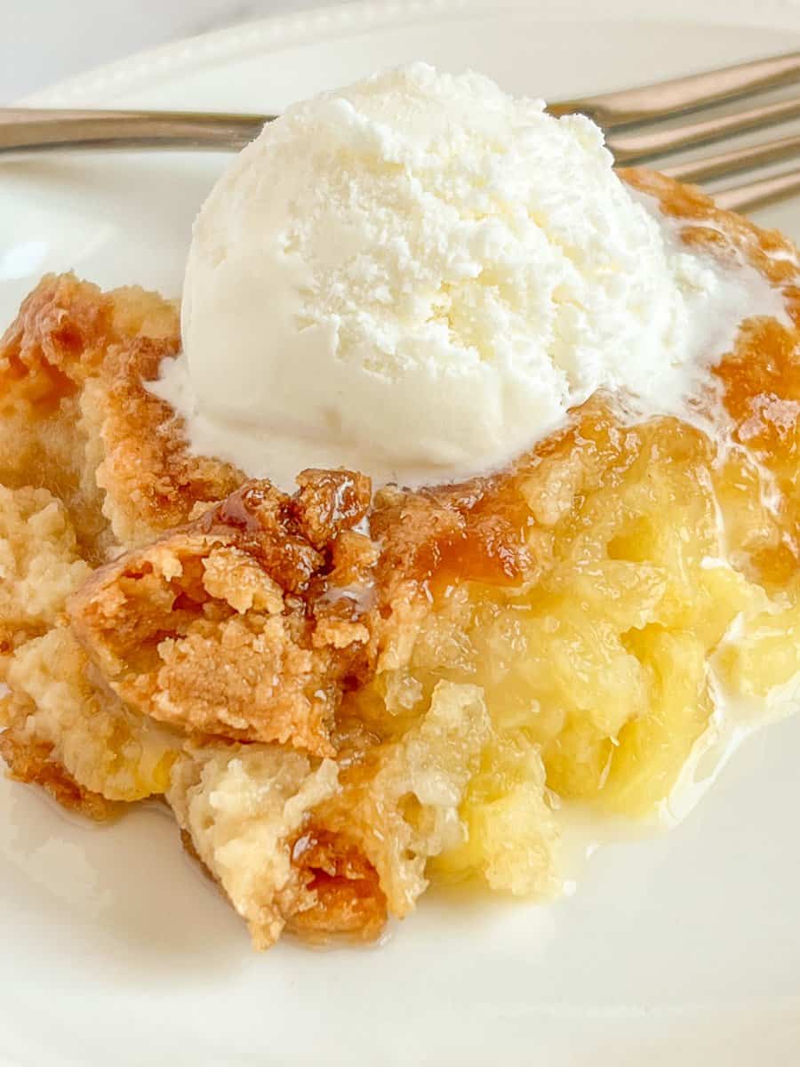 Close up image of pineapple dump cake on white plate with a big scoop of vanilla ice cream.
