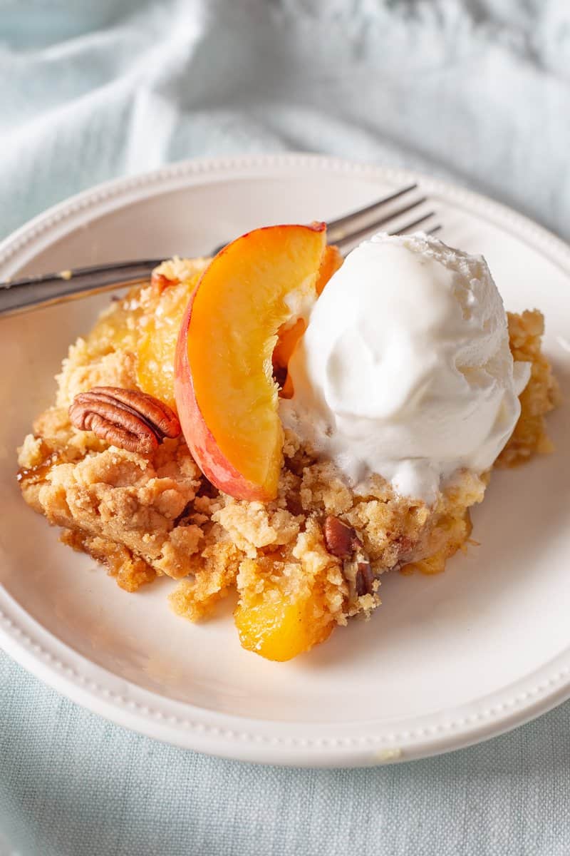 Fresh peach dump cake on white plate with fork and light blue napkin on the side.
