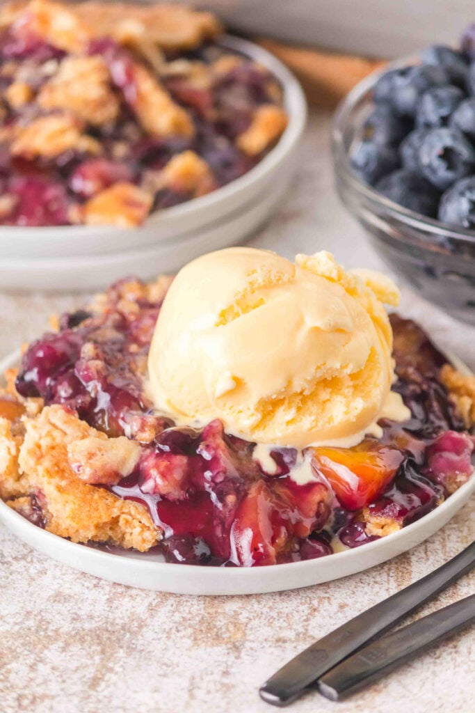 Peach blueberry dump cake serve with vanilla ice cream on a white plate.