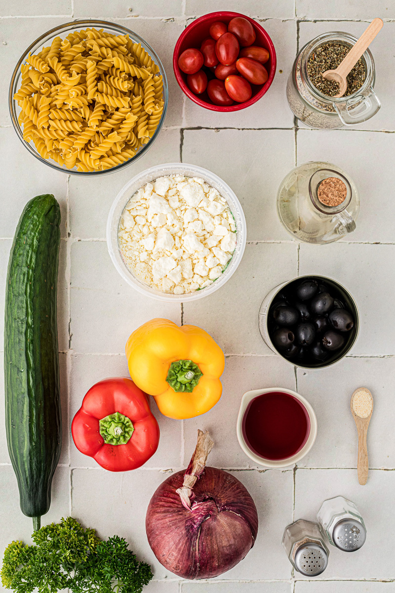 Ingredients for Greek pasta salad in small bowls on counter.