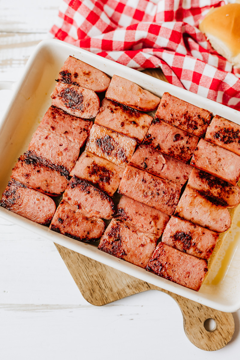 Cooked sausage is sliced and place on top of sliced sliders.