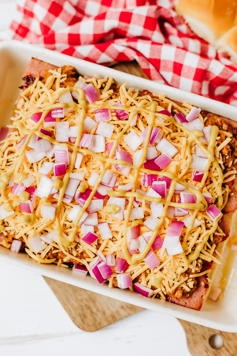 Chopped red onions and mustard are sprinkled on top of the shreded cheese.