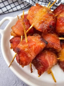 Bacon wrapped pineapple bites on a white plate.