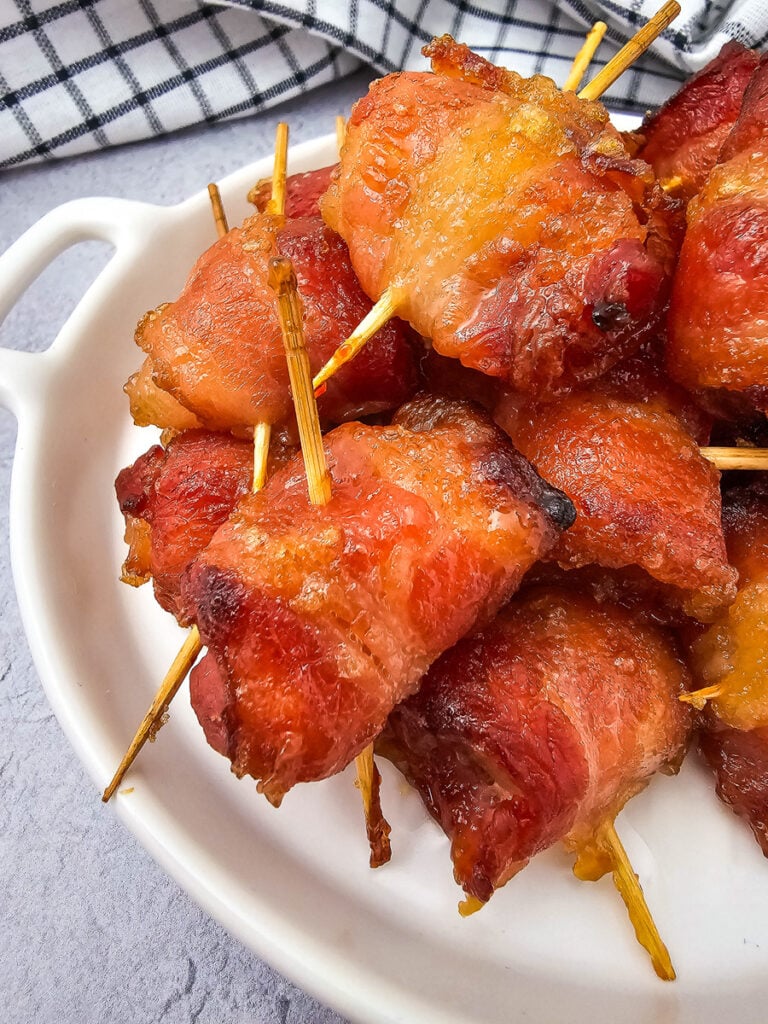 Bacon wrapped pineapple bites on a white plate.