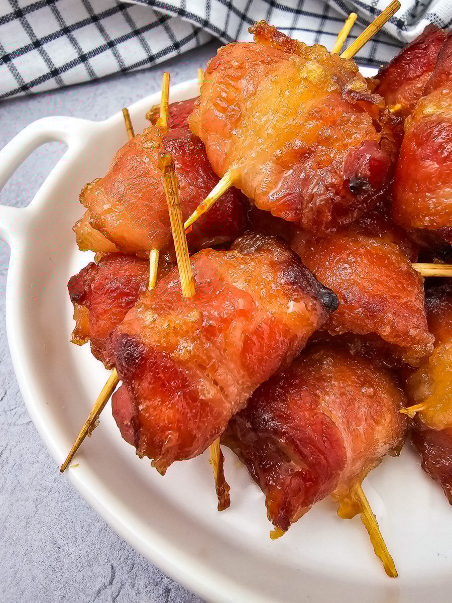 Bacon wrapped pineapple bites on a white plate.
