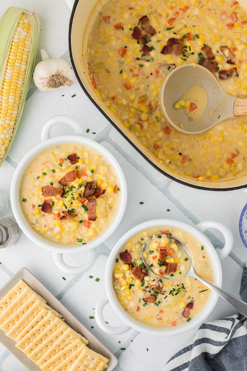 Overhead view of two bowls of corn chowder with soup bowl in background.