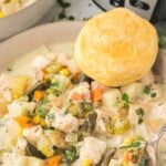 Crockpot chicken pot pie soup in a white bowl with a biscuit on the side.