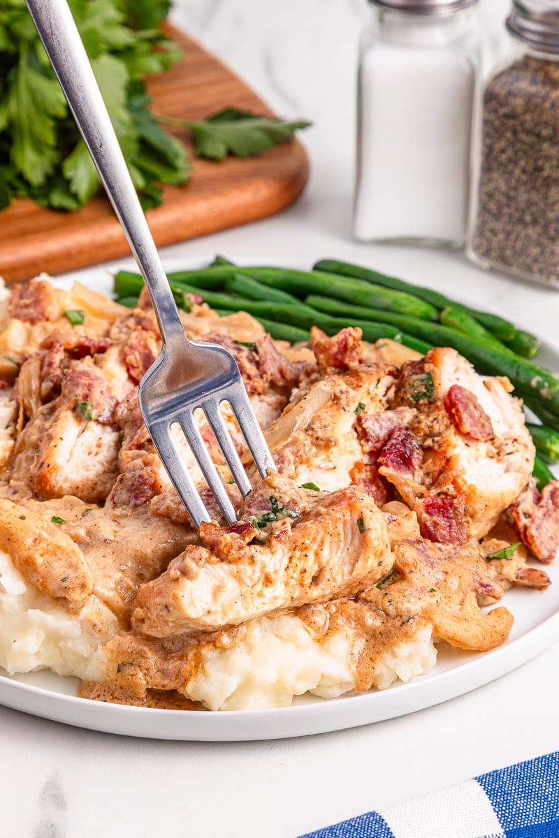 Bite of smothered chicken on fork held over plate.