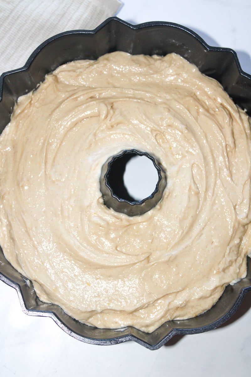 Cake batter is spread on top of apple in bottom of Bundt pan.