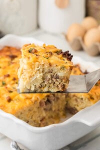 Breakfast casserole with has browns on serving spoon held over baking dish.