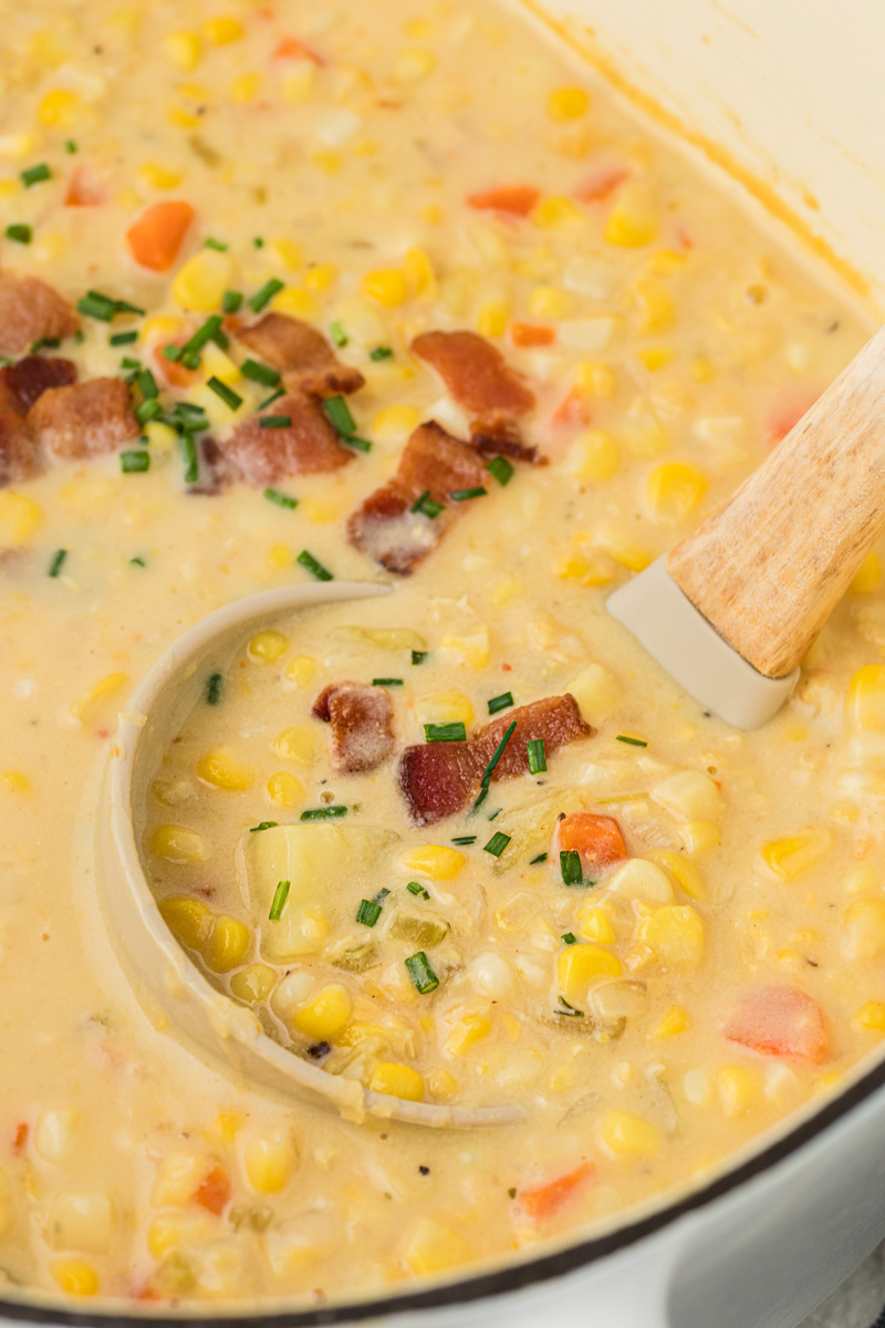 A soup ladle lifting up scoop of corn chowder with bacon.