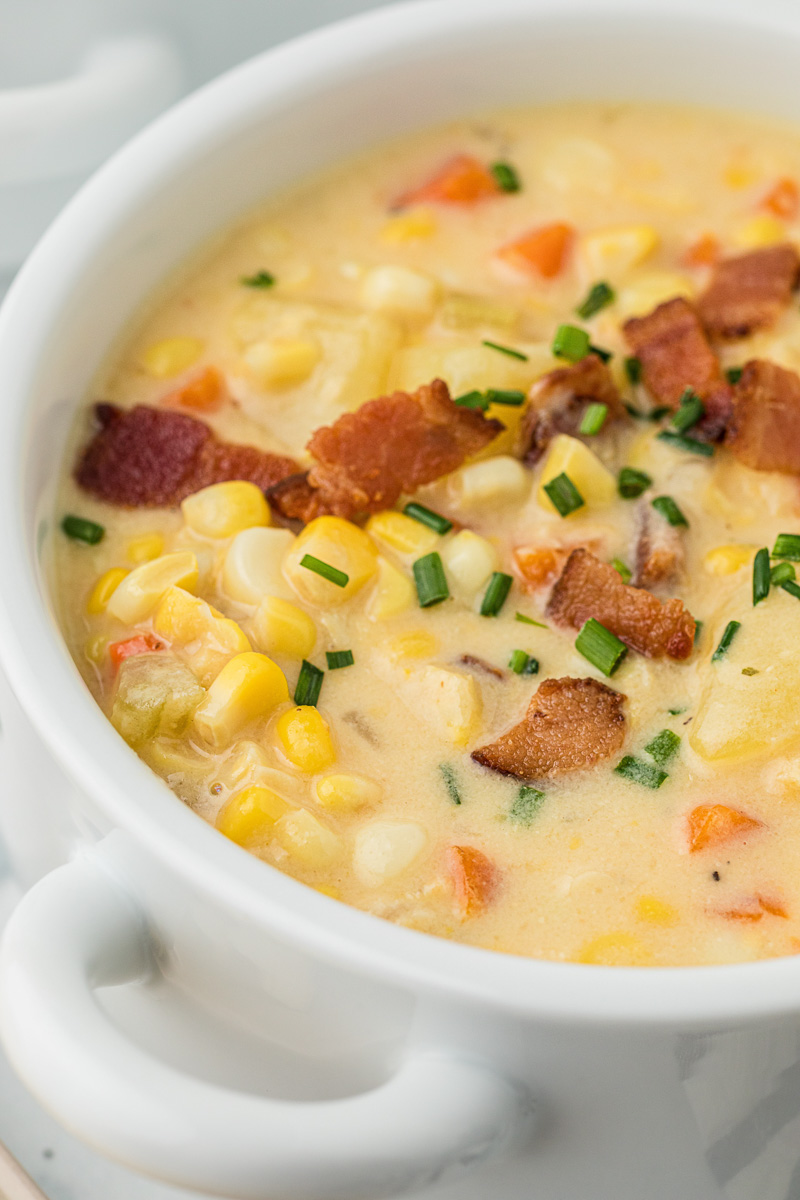 Close up side view of corn chowder with potatoes in a bowl, garnished with bacon.