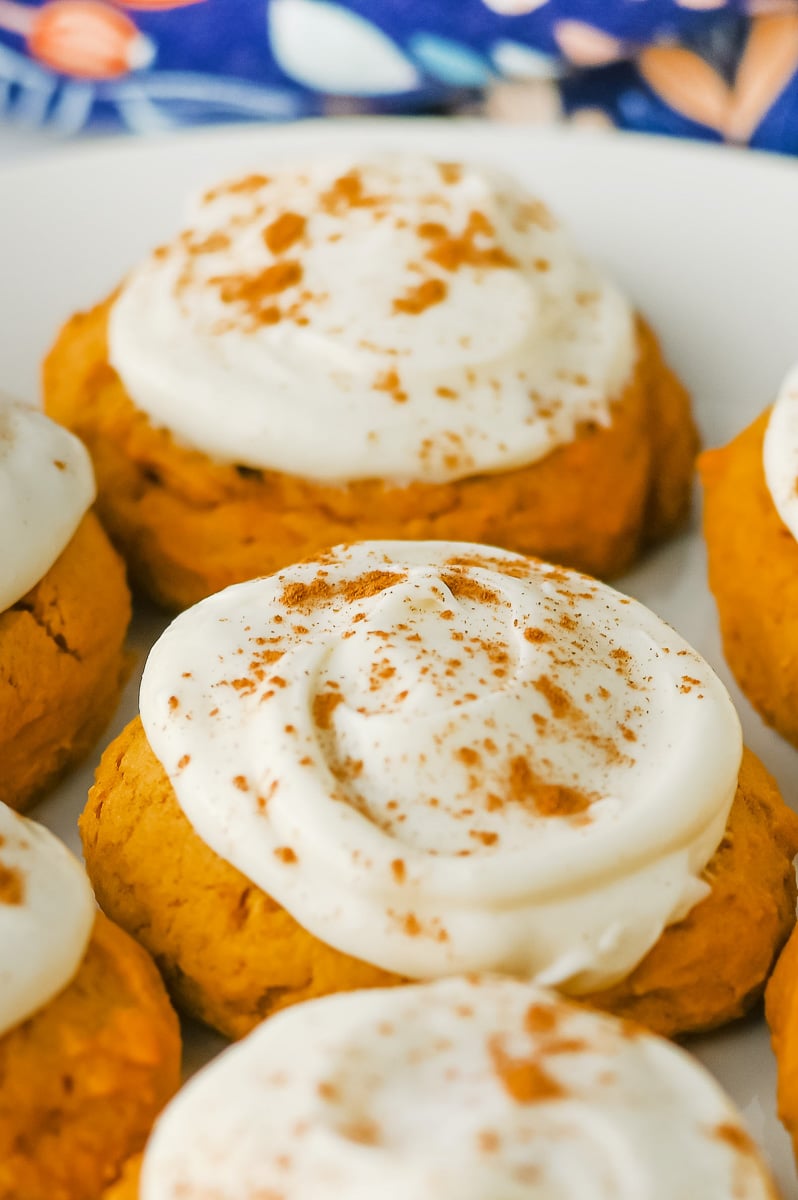 Pumpkin cookies with cream cheese frosting served on a white plate.