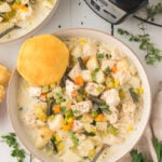 Chicken pot pie soup in a bowl with a biscuit on the side.