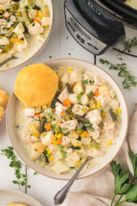 Chicken pot pie soup in a bowl with a biscuit on the side.