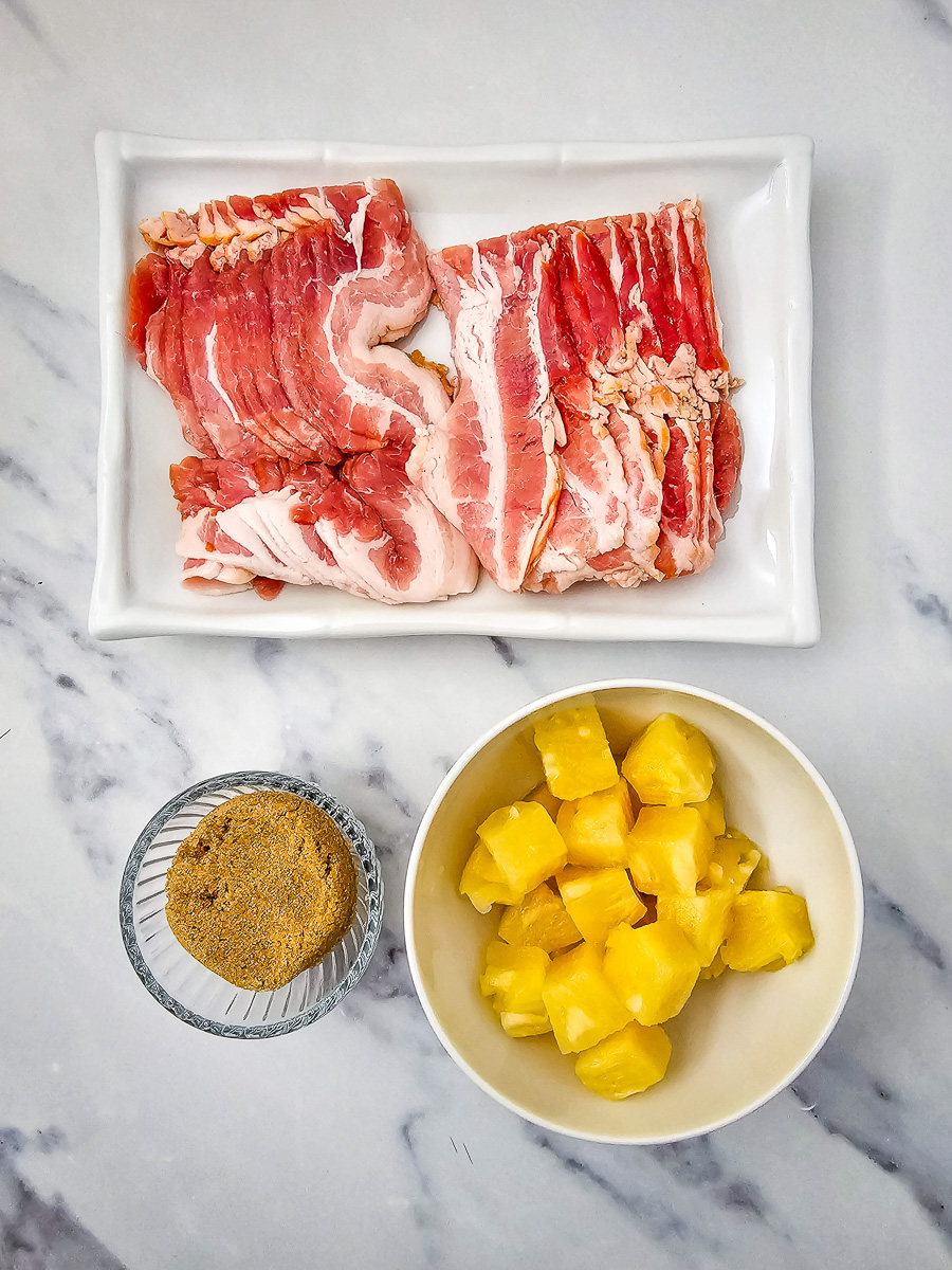 Ingredients for bacon wrapped pineapple bites laid out in small bowls on a counter.