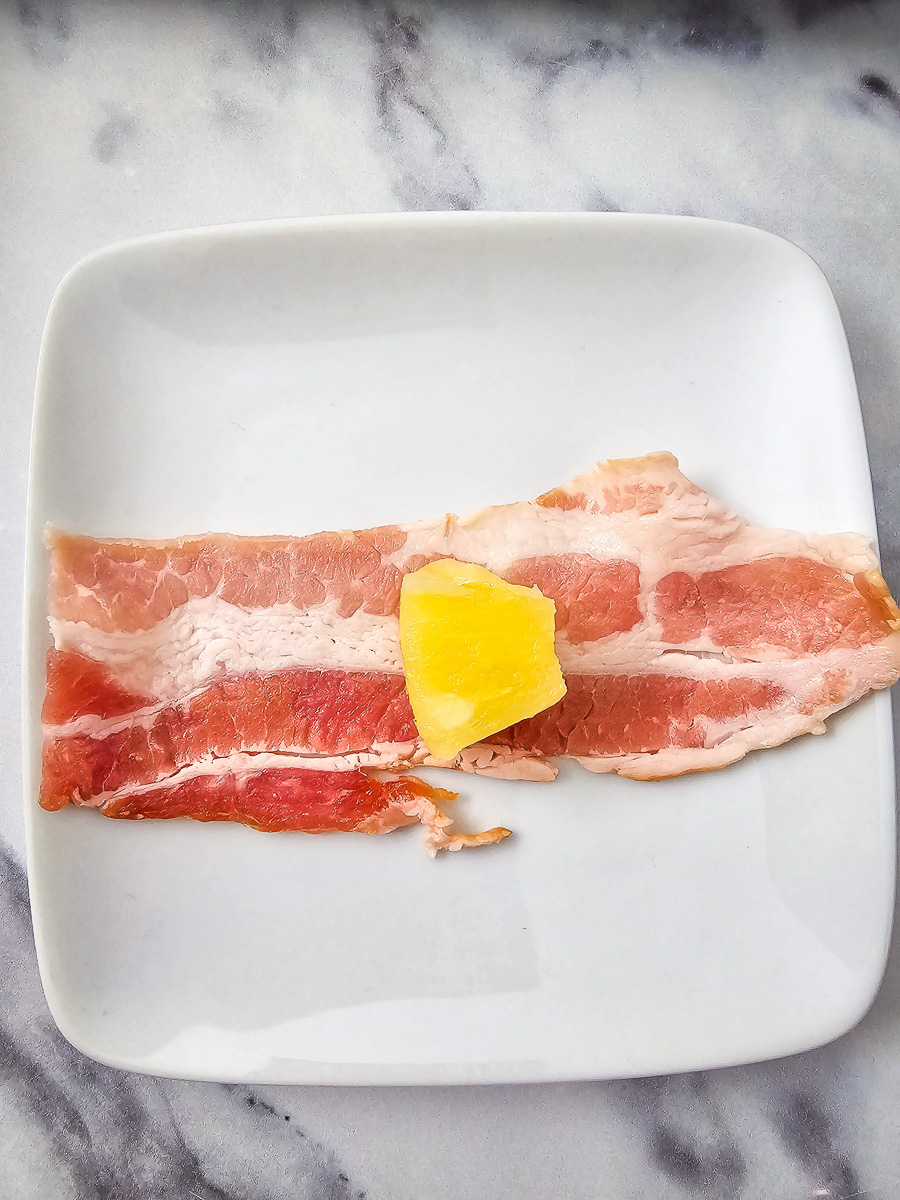 Bacon on plate with pineapple laying on top.