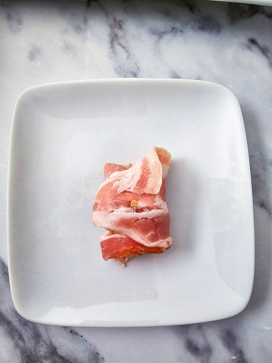 Pineapple wrapped in bacon on a white plate.