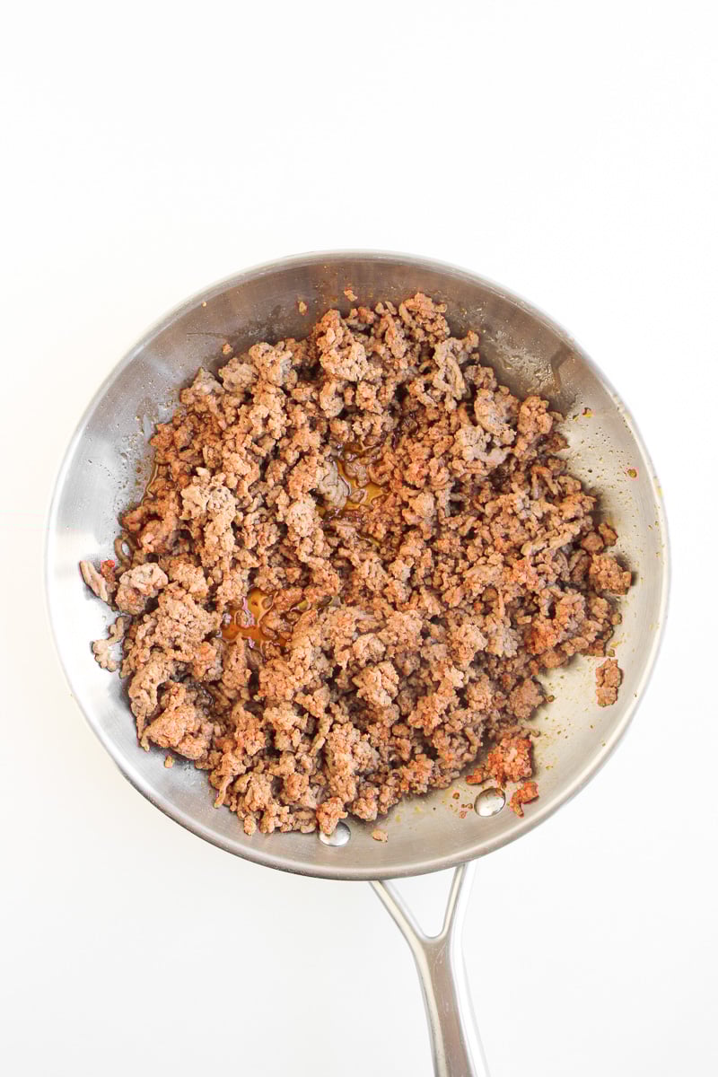 Cooked ground beef in skillet with seasoning.