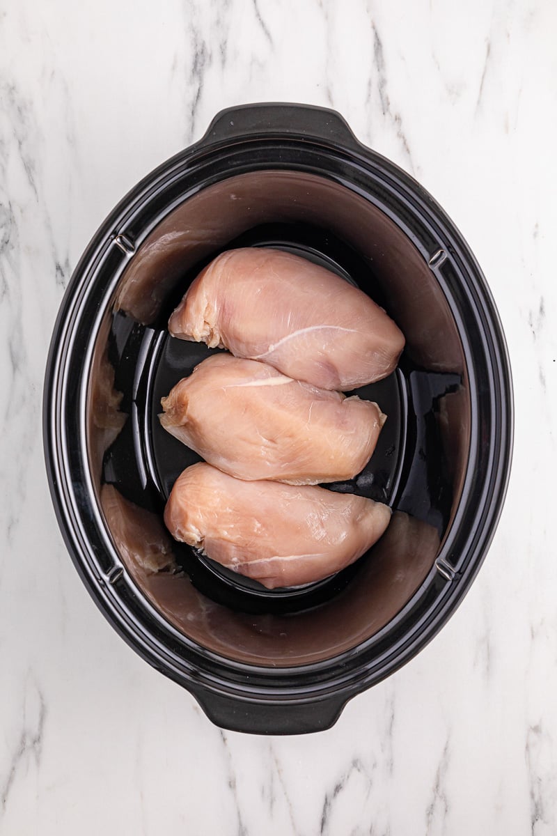 Chicken breasts are placed into the bottom of slow cooker.