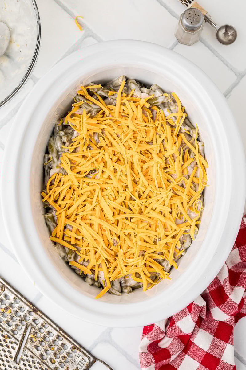 Cheese is sprinkled on top of green bean casserole mixture in crockpot.