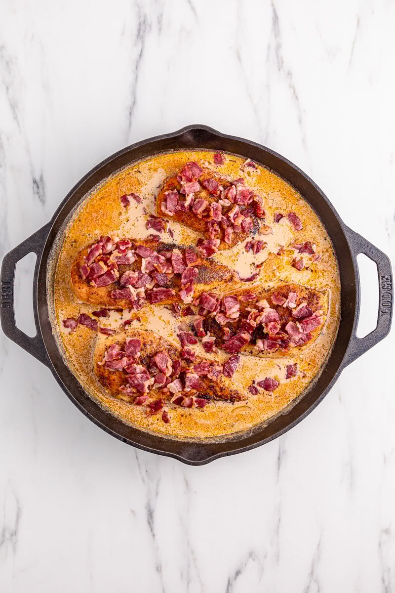 Bacon is sprinkled on top of the chicken in skillet.