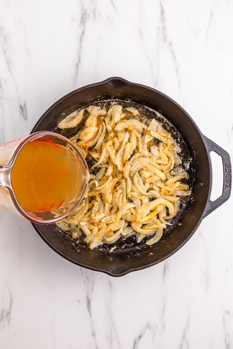 Chicken broth is added to onion mixture in skillet.