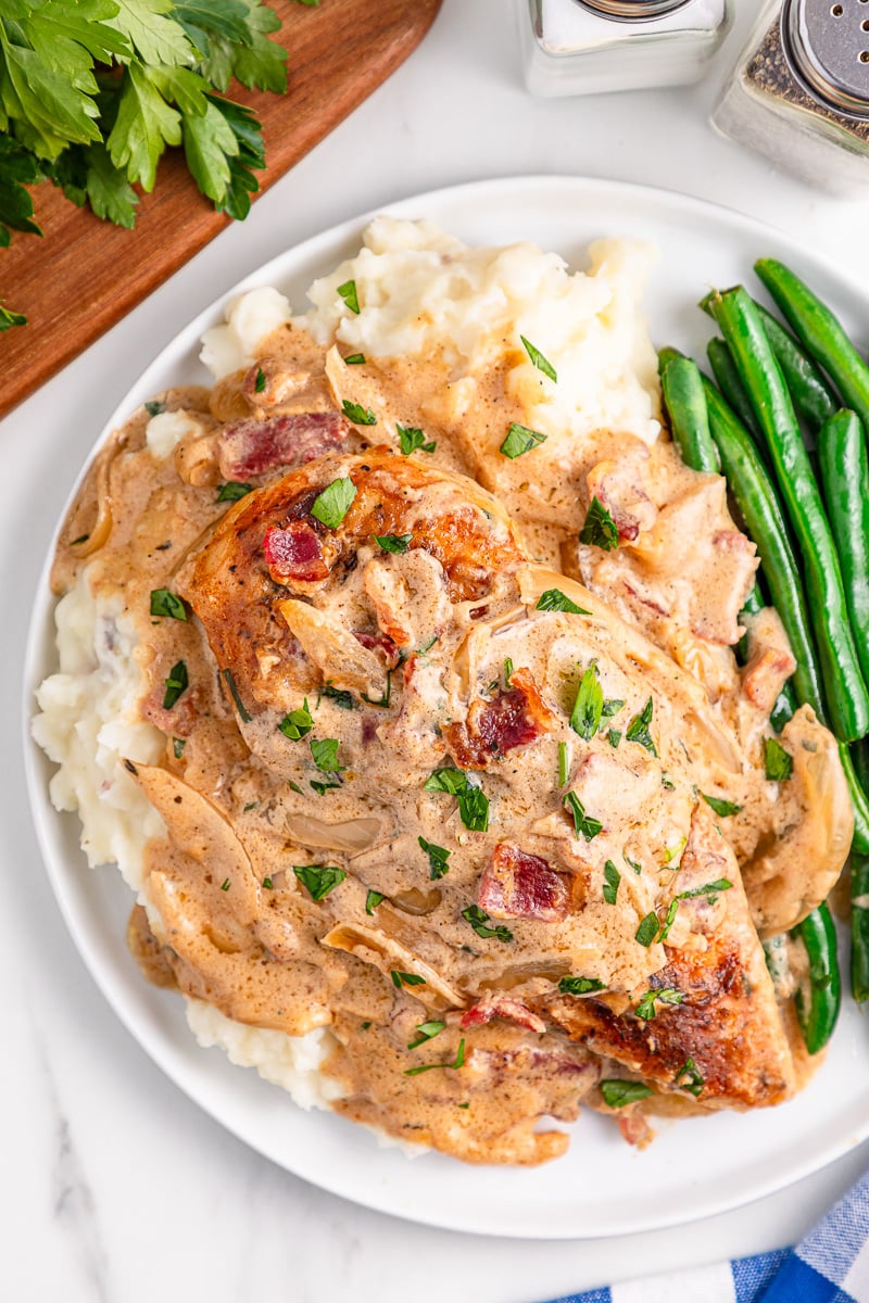 Smothered chicken with gravy served on a plate with mashed potatoes and green beans.