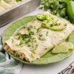 Green chicken enchiladas with sour cream served on a white plate.
