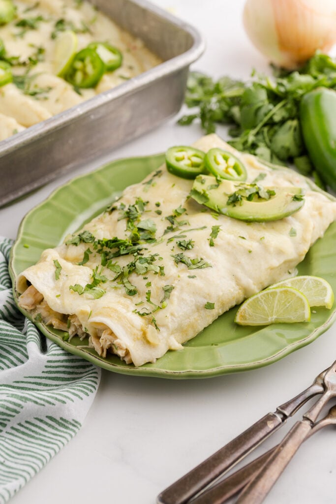 Green chicken enchiladas with sour cream served on a white plate.