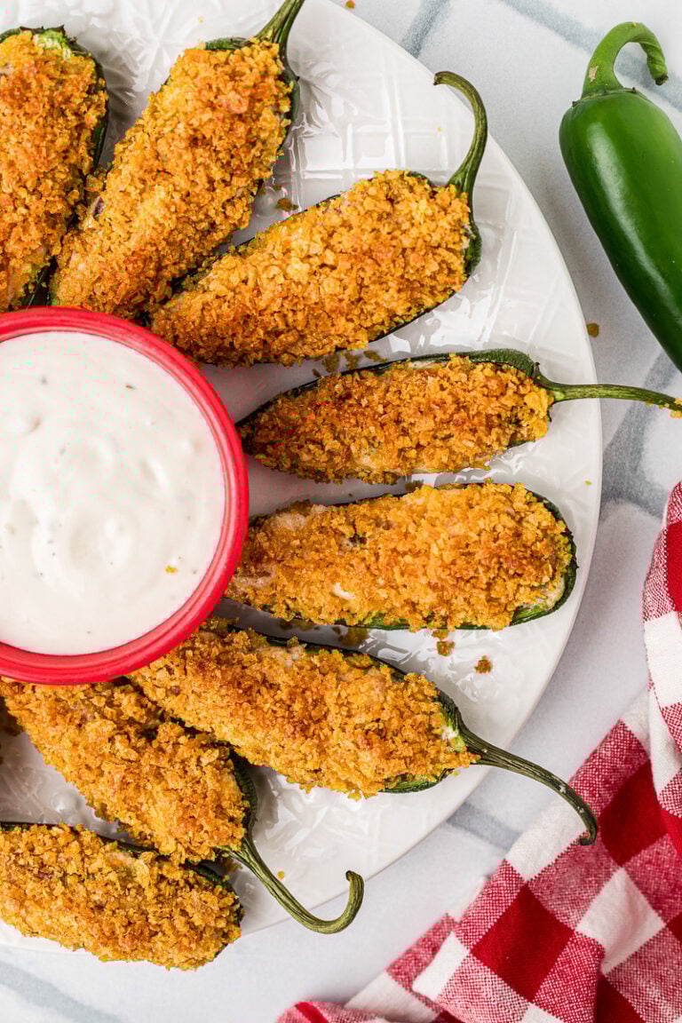 Jalapeno poppers with cream cheese and bacon on a plate with dipping sauce.