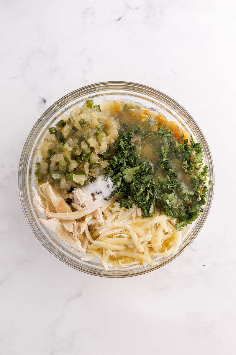 Shredded chicken, 1 cup cheese, cilantro, salt, green chiles, 1 cup enchilada sauce, and the sautéed onion and poblano peppers in bowl.