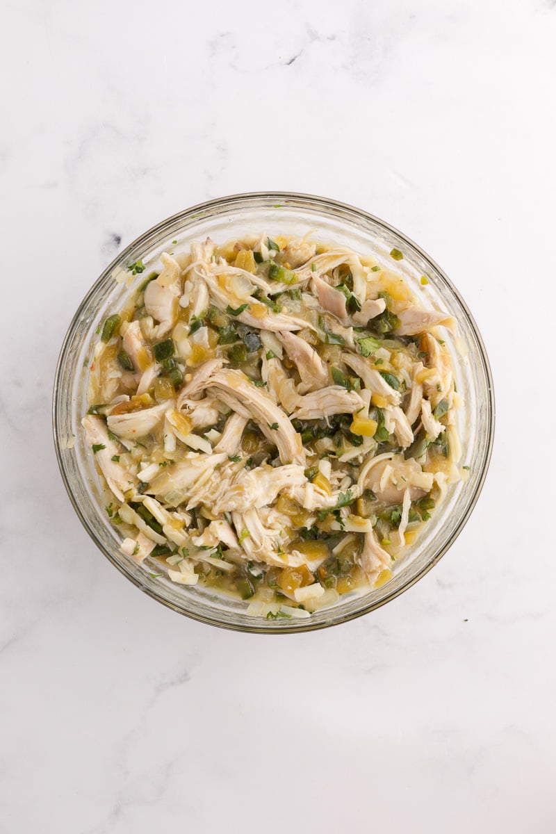 Shredded chicken, 1 cup cheese, cilantro, salt, green chiles, 1 cup enchilada sauce, and the sautéed onion and poblano peppers in bowl stirred.