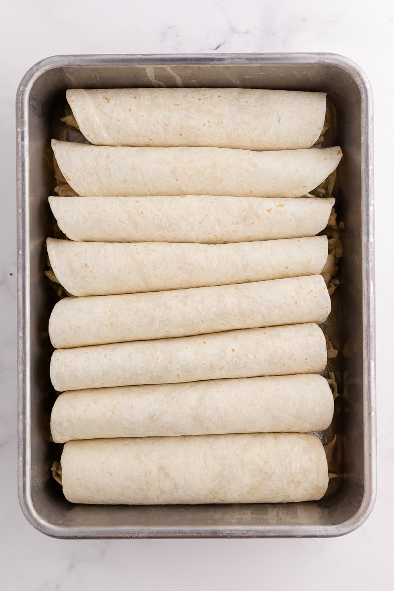 Rolled flour tortillas with chicken mixture placed in baking dish.