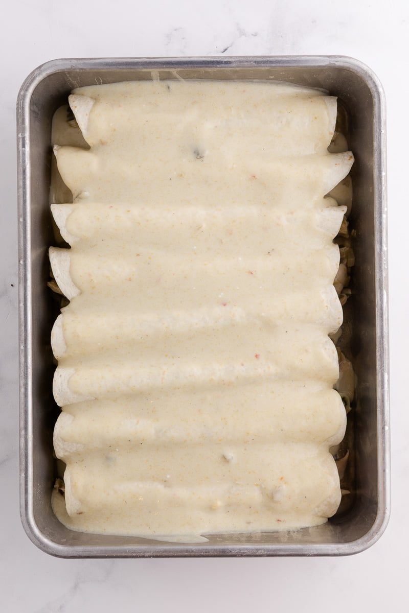 Sauce is spread on top of the enchiladas in baking dish.