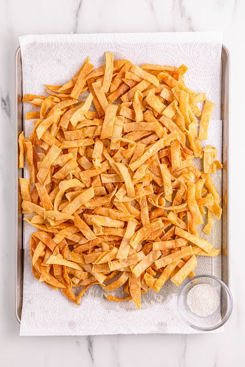 Cruncy tortilla strips draining on paper towelling on baking sheet.