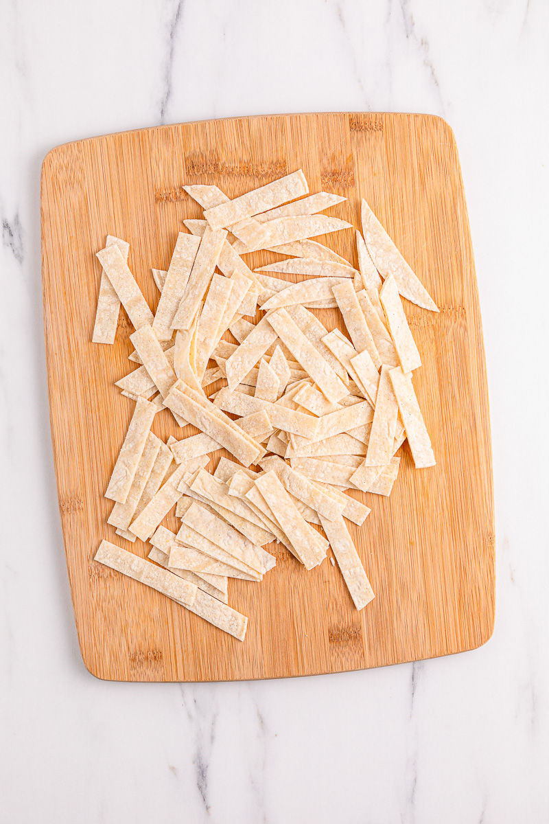Tortillas cut into strips on a wooden cutting board.