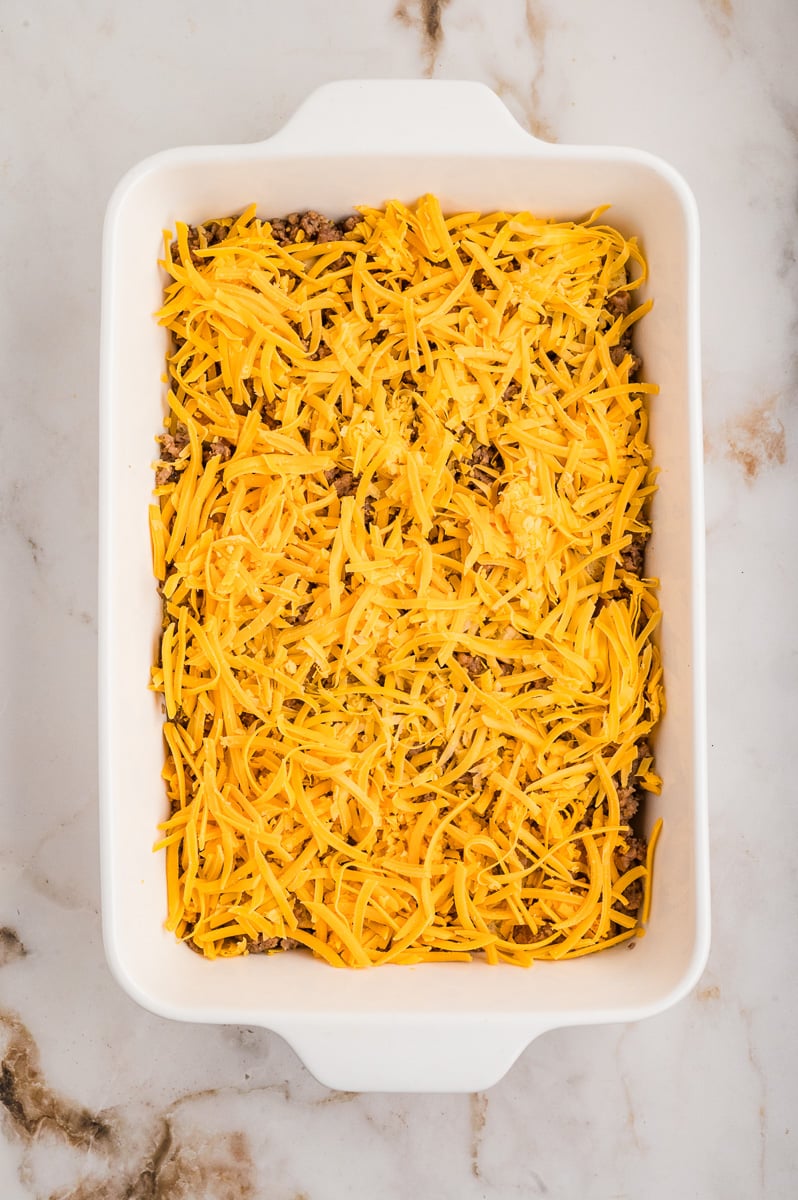 Shredded cheese is sprinkled on top to the sausage mixture in baking dish.