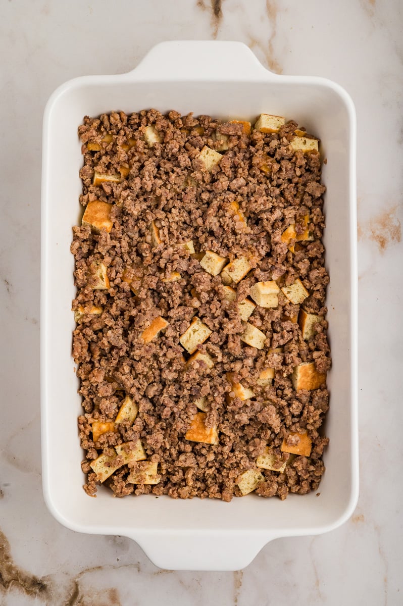 Crumbled cooked sausage is sprinkled on top of the cubed pancakes in baking dish.