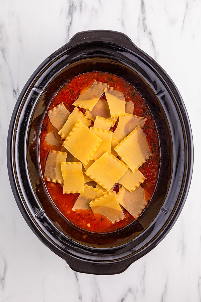 Lasagna pieces are broken into pieces and added to crockpot.