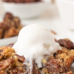 Pecan pie dump cake served on a white plate with vanilla ice cream.
