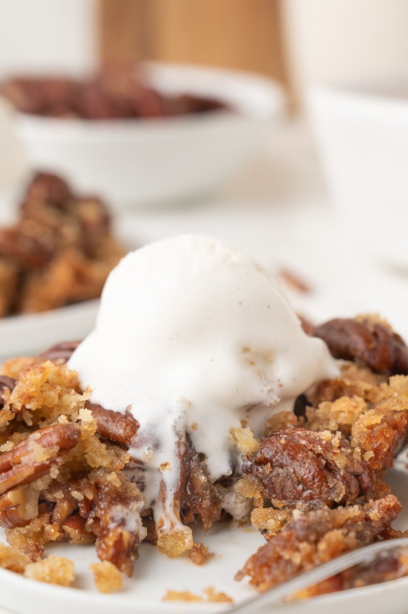 Pecan pie dump cake served on a white plate with vanilla ice cream.