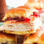 Turkey sliders with cranberry sauce stacked on a plate.
